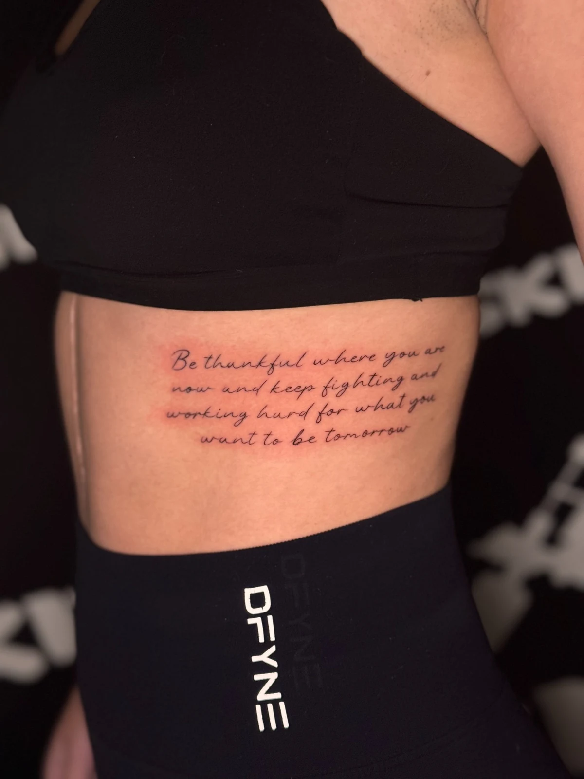 Mehrzeiliger englischer Schriftzug in feiner Schreibschrift auf der seitlichen Rippenpartie – Arbeit von Merci, Skin City Tattoo.